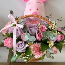Pink plush bunny behind a basket of pastel roses and carnations