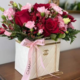 Pink and red flower arrangement in a white Chanel-style box with a ribbon