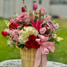 Pink and red mixed flower arrangement in a wicker basket with a pink ribbon