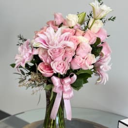 Pink roses and lilies arranged in a tall glass vase with a pink ribbon