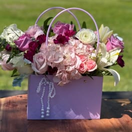 Pink and white flower arrangement in a lavender gift bag with pearl trim