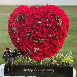 Heart-shaped red rose and carnation arrangement in a black box with anniversary text
