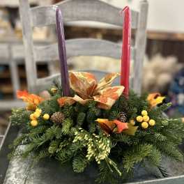 Evergreen centerpiece with fall ribbon, berries, and two taper candles on a metal tray