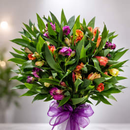 Bouquet of multicolored flowers in a white vase with a purple ribbon