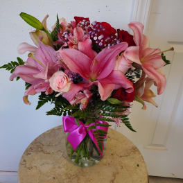 Pink lilies and roses in a glass vase with a magenta ribbon