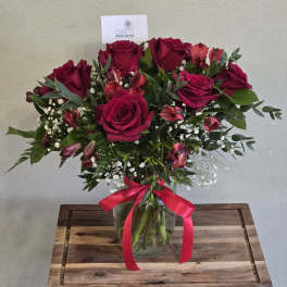 Bouquet of deep red roses and pink alstroemeria in a glass vase with a ribbon