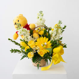 Yellow teddy bear in a basket with yellow and white flowers