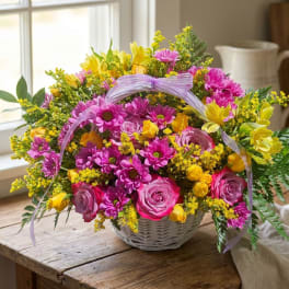 Basket arrangement of pink and yellow flowers with a lavender ribbon