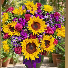Bouquet of sunflowers, pink roses, and purple filler flowers in a vase