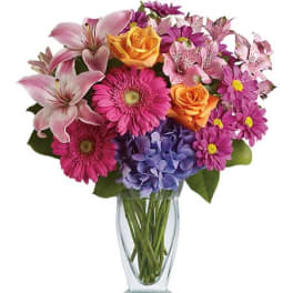 Mixed bouquet of pink lilies, roses, daisies, and hydrangea in a glass vase