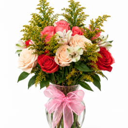 Bouquet of pink, red, and peach roses in a glass vase with a pink bow
