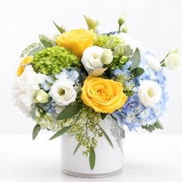 Yellow and white roses with blue hydrangeas in a clear vase