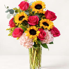 Bouquet of pink roses, sunflowers, and pale hydrangeas in a clear glass vase