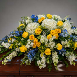 Yellow roses and white flowers arranged on a casket with blue accents