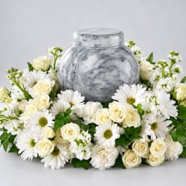 White roses and daisies arranged around a gray urn