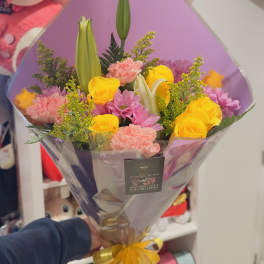 Bouquet of yellow roses, pink carnations, and lilies wrapped in purple paper