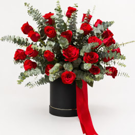 Red roses in a black hatbox with eucalyptus and a red ribbon