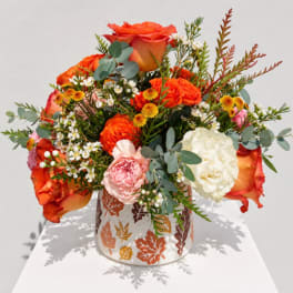 Orange roses and mixed blooms in a leaf-patterned vase