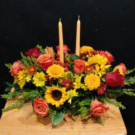 Floral centerpiece with roses, sunflowers, and two taper candles