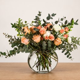 Peach and white roses in a round glass vase with eucalyptus