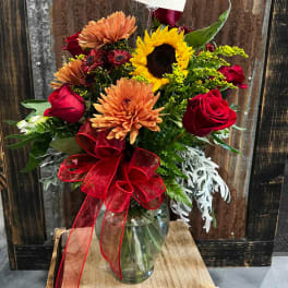 Bouquet of sunflowers, roses, and mums in a glass vase with a red ribbon