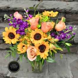 Bouquet of peach roses, sunflowers, and purple flowers in a glass vase