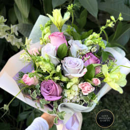 Handheld bouquet of pastel roses and pale yellow flowers wrapped in white paper