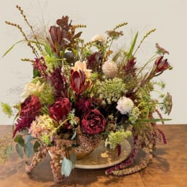 Large burgundy and blush floral arrangement in a low bowl on a wooden table