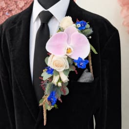 Pink orchid boutonniere with cream roses and blue flowers on a black suit lapel