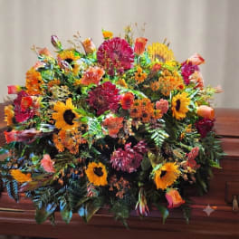 Large colorful floral casket spray with sunflowers, roses, and mums