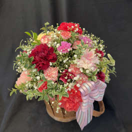 Mixed bouquet of red, pink, and white carnations in a basket with a ribbon
