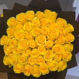 Bouquet of bright yellow roses wrapped in dark paper
