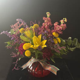 Colorful mixed bouquet in a red glass vase with a rainbow ribbon