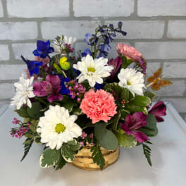 Mixed bouquet in a woven basket with white daisies, pink carnations, and purple blooms