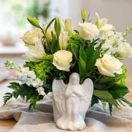 White roses and lilies arranged in a white angel vase