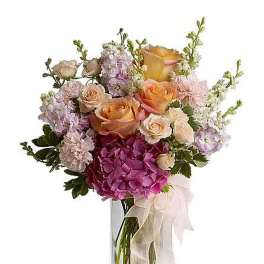 Tall vase arrangement of peach roses, pink hydrangea, pale carnations, and pastel flowers with a ribbon bow