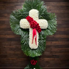 White floral cross with red roses and ribbon on a palm backdrop