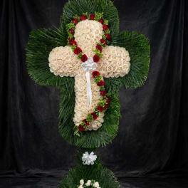 Cross-shaped floral tribute with cream roses, red roses, and white bows
