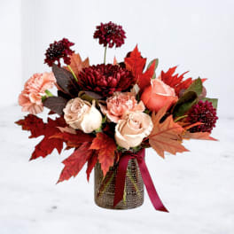 Autumn bouquet of roses and carnations in a textured vase with a ribbon