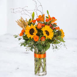 Sunflower and orange rose arrangement in a tall glass vase with an orange ribbon