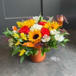 Bouquet of sunflowers, red roses, and white alstroemeria in an orange vase