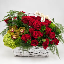 Red roses and orchids arranged in a white basket with a ribbon