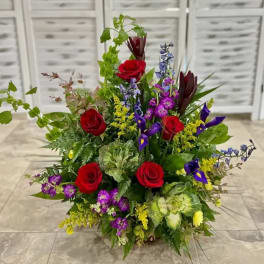 Tall mixed bouquet with red roses, purple flowers, and green accents in a low container.