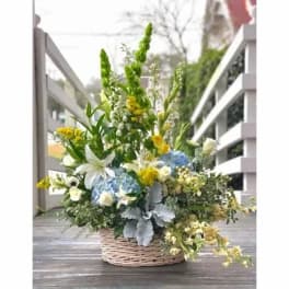 Basket arrangement with white lilies, blue hydrangeas, and yellow flowers