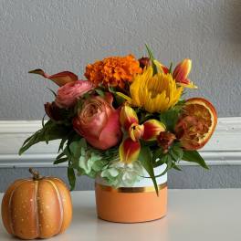 Autumn bouquet in a peach vase with a small decorative pumpkin beside it.