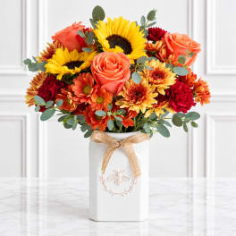 Bouquet of sunflowers, roses, and mums in a white vase with a ribbon