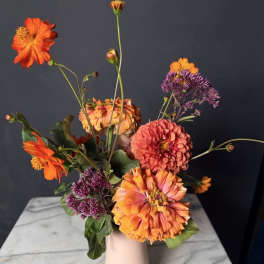 Orange and pink flowers arranged in a pale vase