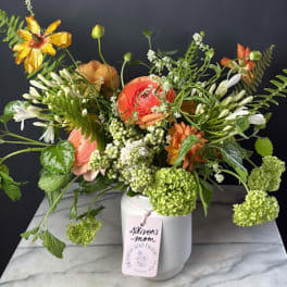 Mixed bouquet in a white vase with coral, white, and green blooms
