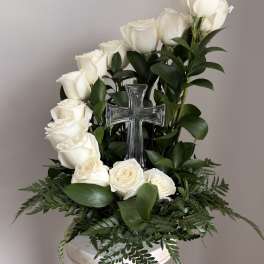 White roses arranged around a clear glass cross on a pedestal stand