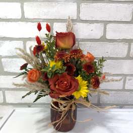 Mixed bouquet of red and orange roses with yellow daisies in a brown vase